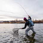 Person fly fishing in a body of water with a backpack and waders and landing net (global).